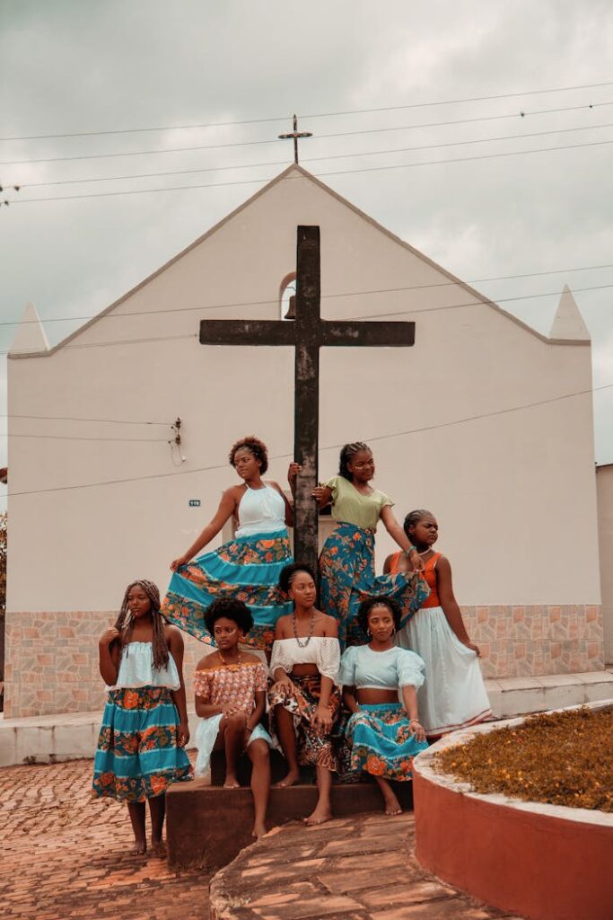 Fashionably dressed women posing in front of a cross on a village church building.