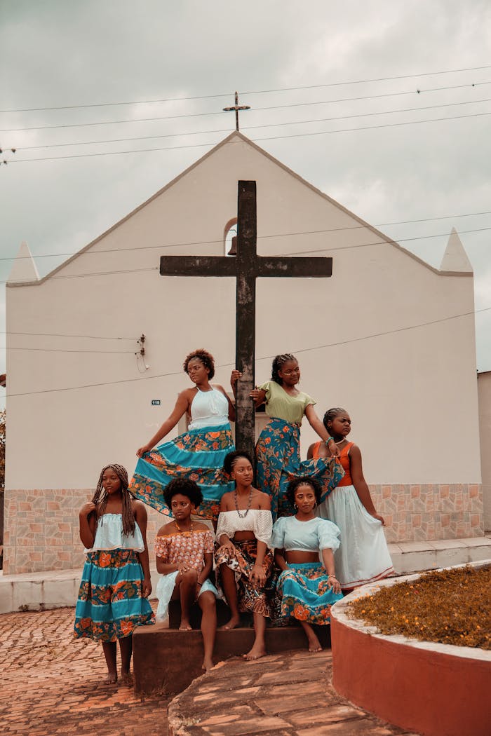 Fashionably dressed women posing in front of a cross on a village church building.